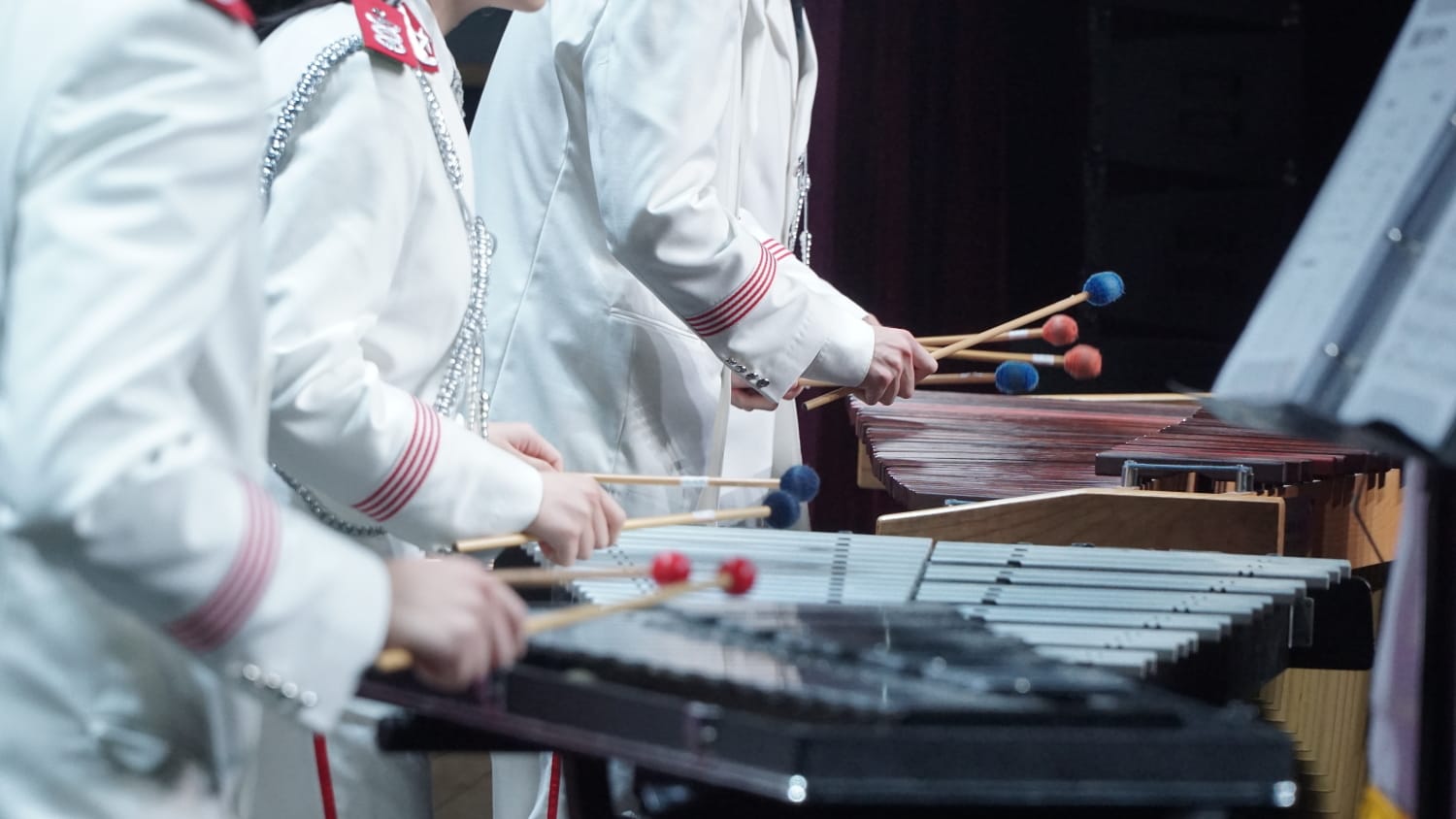 低角度侧视照片，黑色背景的舞台上，白色制服的乐队成员手持琴槌演奏。