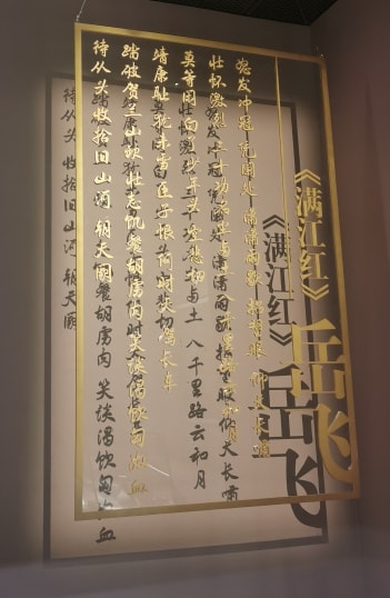 岳飞《满江红》以金黄色文字印于透明板上垂直放置，由柔光暖色灯在背后的墙上映出影子，墙面如同古籍一页，文字也如同从古籍中浮现到眼前一般。