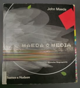 放在桌上的《MAEDA@MEDIA》书籍封面，灰黑色背景上点缀着少许色块与线条，以白色像素字体写着书名。