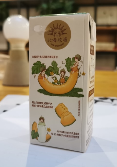 桌上的牛奶盒，其上绘制的插图是橙色的蜜瓜与周围的人物。