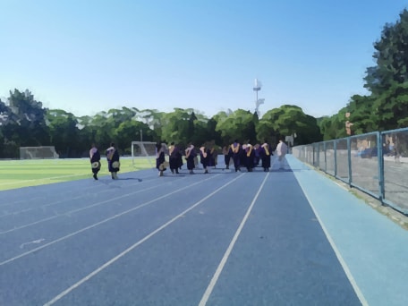 模糊的照片。操场上毕业生们手持乐器沿跑道前行的背影。
