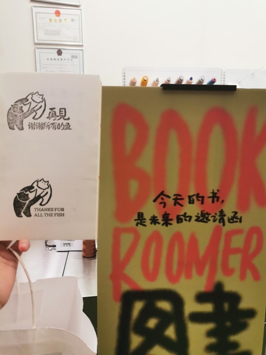 盖有汉英双语“再见，谢谢所有的鱼”纪念章的书页，一旁是“图书房客”的海报，上面写着“今天的书，是明天的邀请函”。