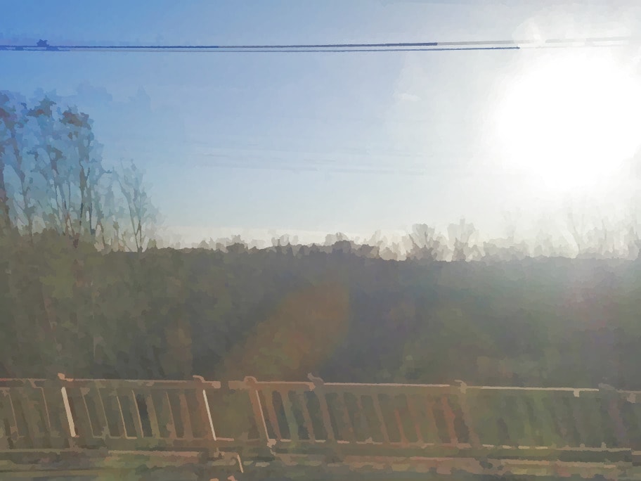 火车车窗外的景色，蓝天下长满树木的平原，由木质栏杆与火车相隔。照片经模糊处理。